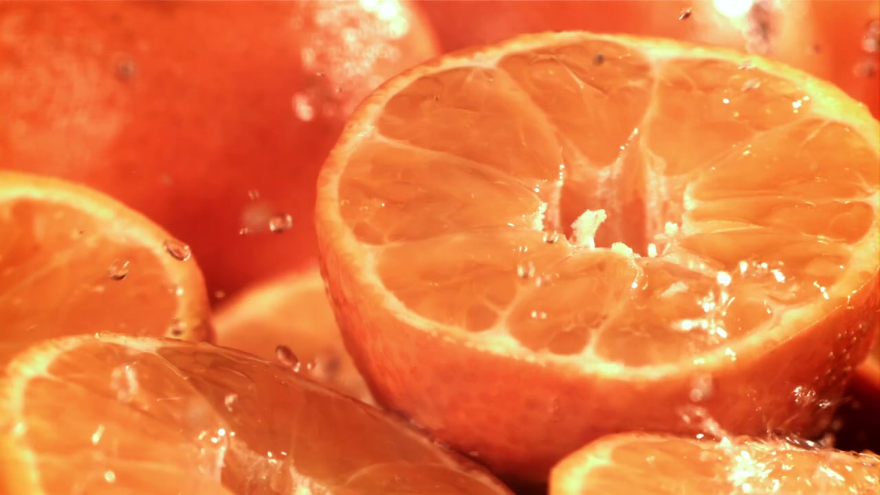 Erfrischendes Wasser spritzt in Zeitlupe auf leuchtende Orangenhälften