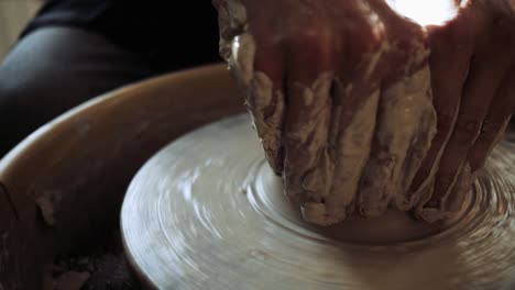 manos de un joven alfarero trabajando en la rueda de un alfarero y haciendo una olla