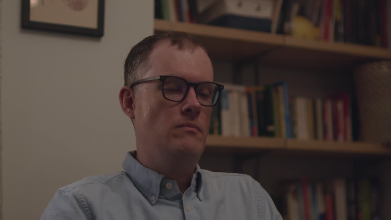 A frustrated office worker taking off his glasses, rubbing his brow, leaning back in his chair, taking a breath, and returning to work