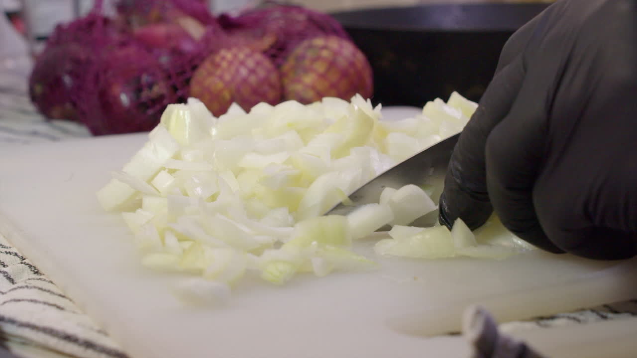 White onion sliced, diced with knife on cutting board by gloved hands