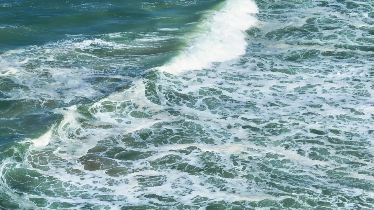 Waves crash on the sandy beach along the Atlantic coast. Aerial view shows the coastline and shoreline. Ocean water reflects sunlight. Coastal dunes outline the beach area.