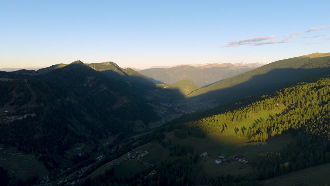 Cinematic aerial view of Dolomites Italy at sunrise, rugged rocky peaks above lush alpine hills and scattered chalets, serene mountain travel landscape nature scenery
