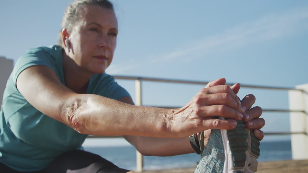mujer mayor estirando sus piernas en un paseo marítimo