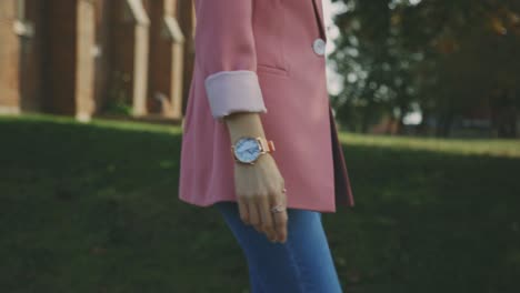 dama en su traje rosa y atuendo de jeans azules con elegante reloj de pulsera camina en el paisaje borroso del prado