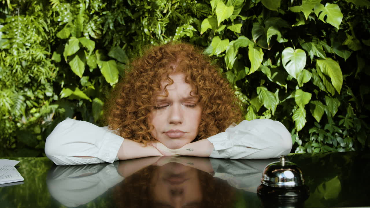 уставшая рыжеволосая рецепционистка за прилавком.