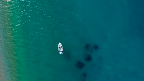 barco flotando en aguas cristalinas de color turquesa cerca de una playa prístina donde la gente toma el sol en el mediterráneo