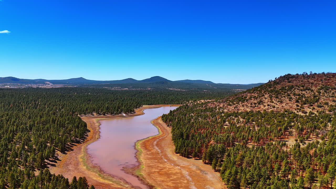 Dried out river surrounded by the pine tree woods. Mountain range at backdrop. Aerial view. Arizona, USA