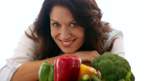 bonita morena sonriendo a la cámara detrás de las verduras