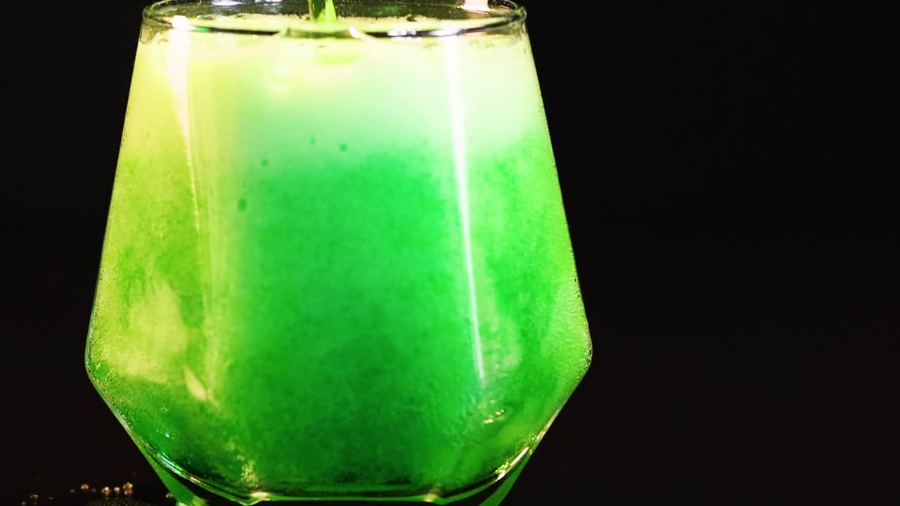 A sequence of green liquid foaming in a hexagonal glass against a dark background.