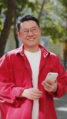 a smiling man in a red jacket holds a phone