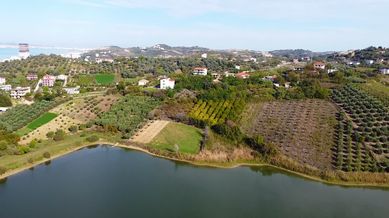 Aerial above agricultural fields and houses in Golem, Albania, view on lake Golemit.