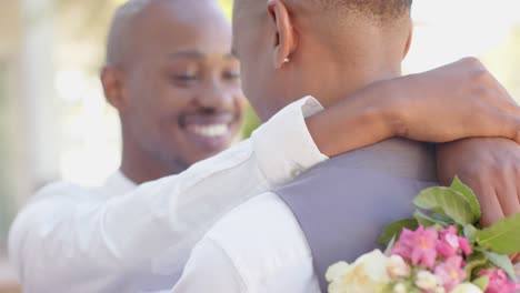 happy african american gay male couple holding flowers and embracing at wedding, slow motion