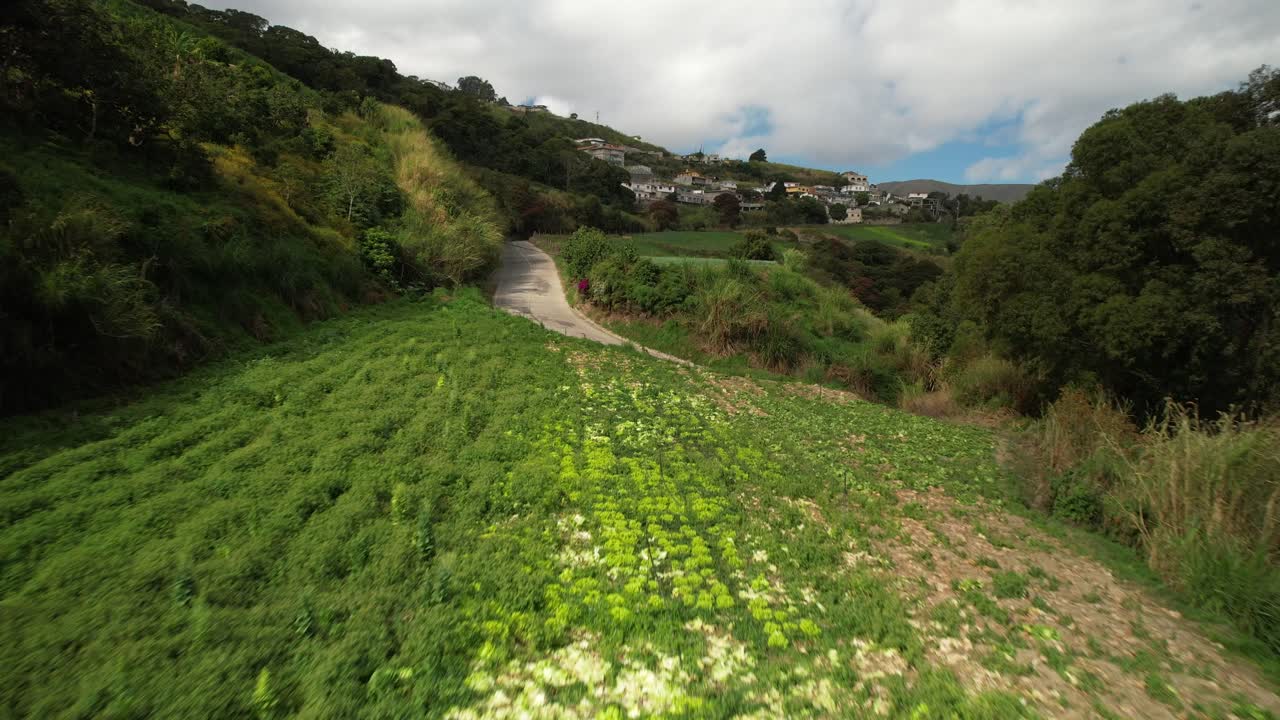 Aerial view over green hills leading towards a residential area in the distance