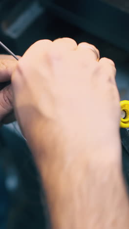 cu shot: skilled jeweler coils thin gold wire on metal pin by hands at workplace in traditional workshop closeup