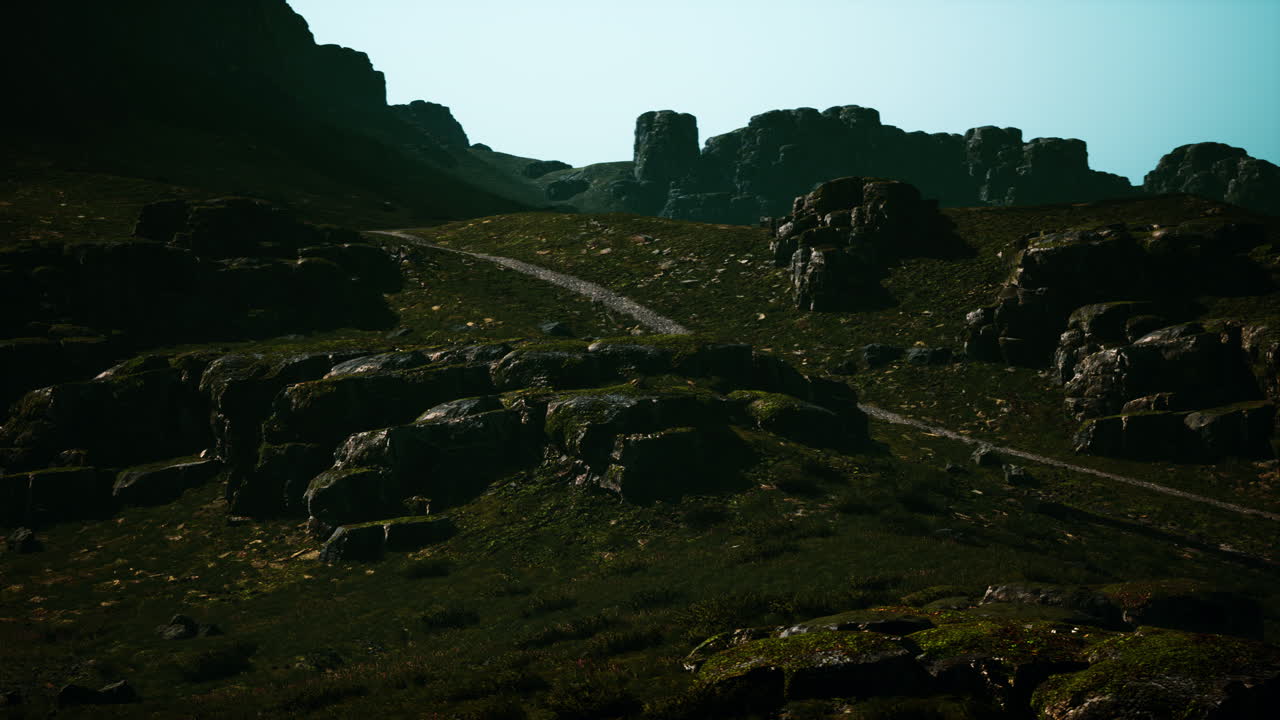 un sendero sinuoso conduce a través de un exuberante paisaje montañoso verde, con altas formaciones rocosas en el fondo.