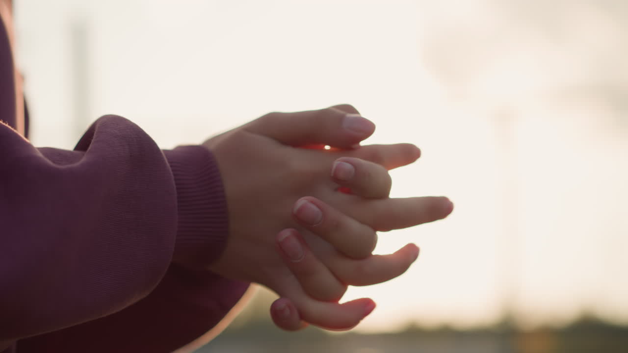 은색 옷을 입은 여성 손의 클로즈업, 손가락이 함께 인 손목을 회전시키고, 빛이 손을 둘러싸고 반이는 효과를 만들어, 따뜻함, 운동 및 체력 활동을 강조합니다.