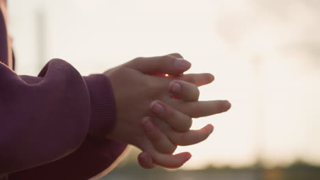 close-up of woman hands in maroon clothing making wrist twist with fingers locked together, sunlight creating a glow effect around hands, emphasizing warmth, movement, and fitness activity