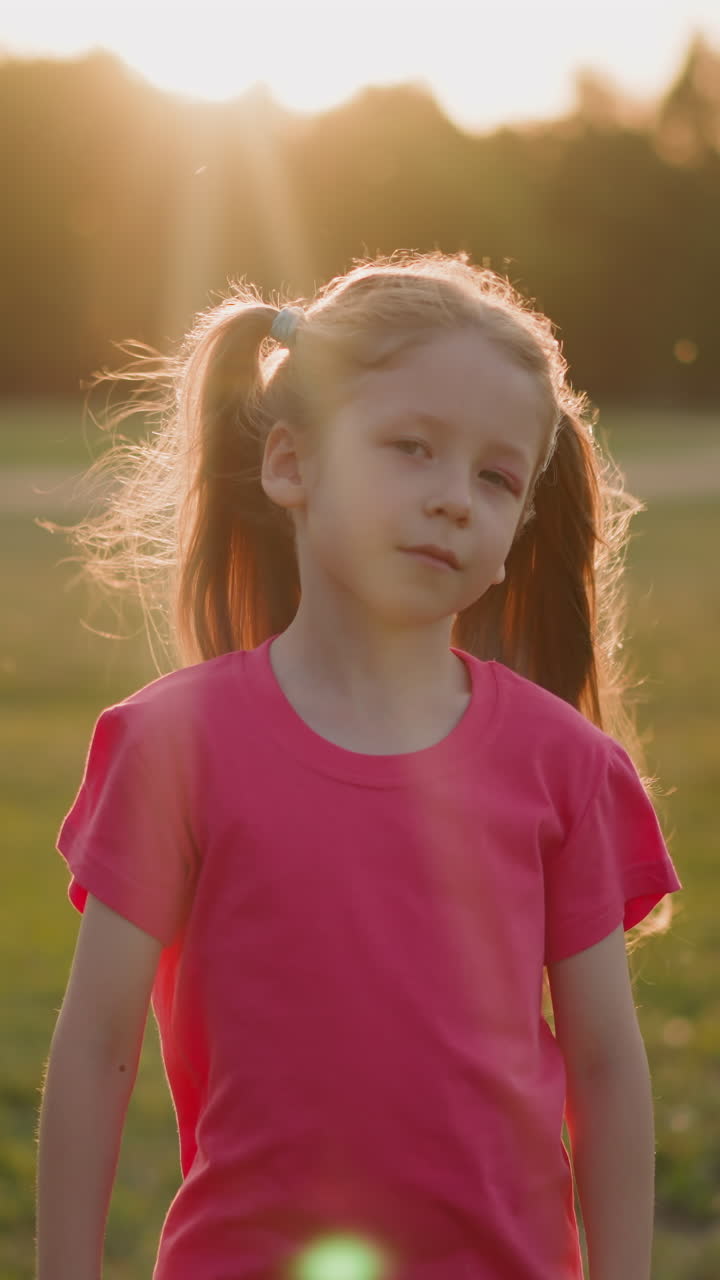 Cute little girl with blonde ponytails waving in wind turns on meadow at sunset slow motion. Playful child in windy evening. Childhood and enjoyment