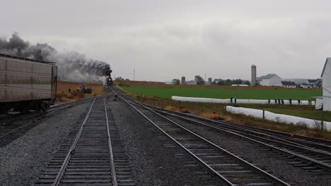 cabeza a la vista de una locomotora de vapor tirando de la carga tirando hacia el patio con humo y vapor en un día lluvioso