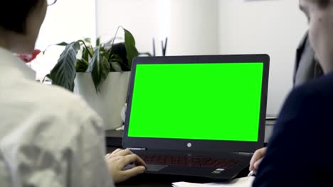 dos personas mirando una computadora portátil con una pantalla verde