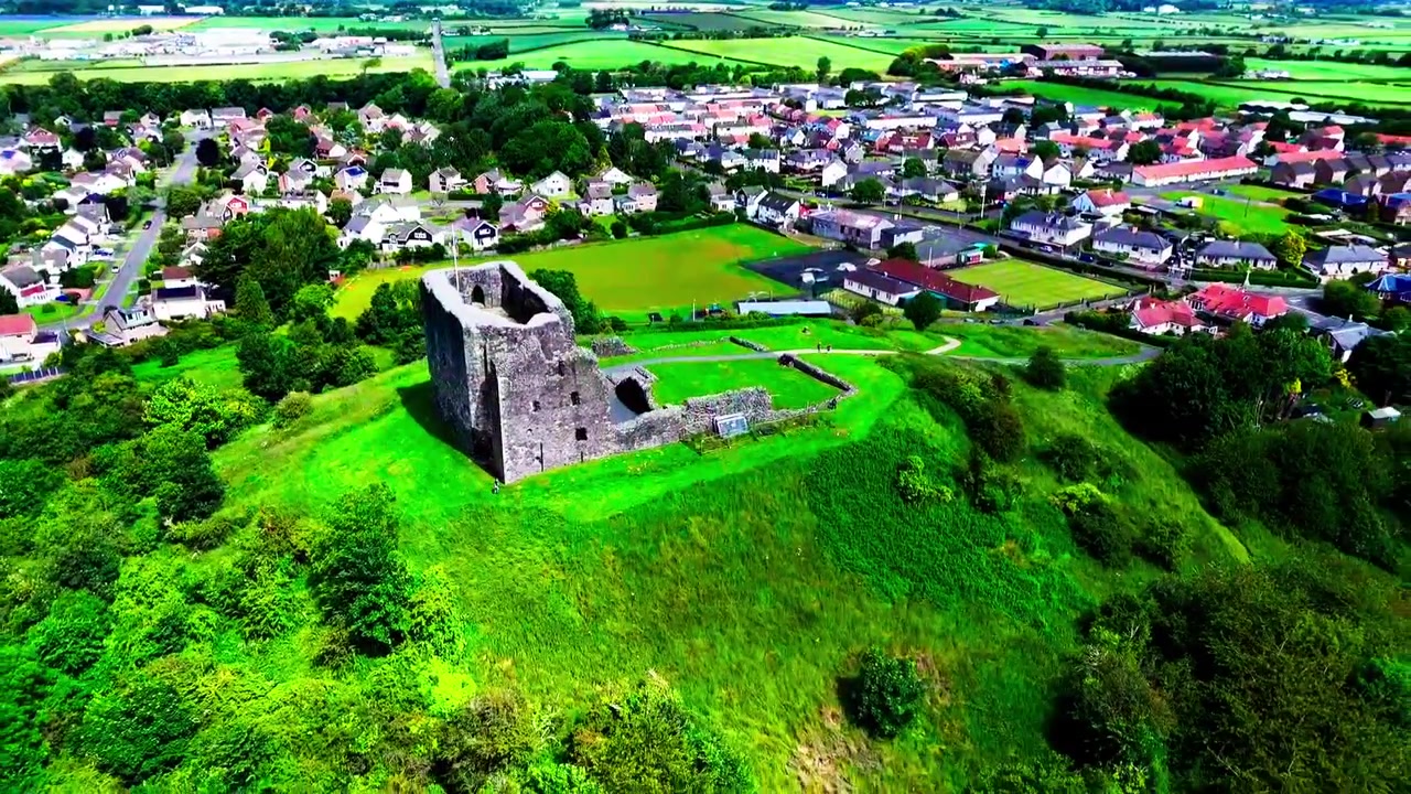 Ladera del Castillo de Dundonald rodeada de bosques, edificios de pueblo y campiña ondulada en Ayrshire, Escocia, vista aérea cinematográfica