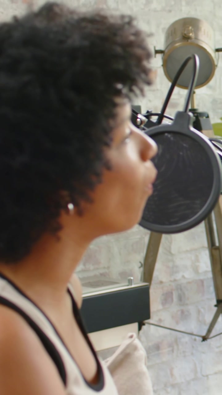 Vertikal video: Syngende kvinde i tanktop indspiller vokal på hjemmesofa med mikrofon, plads til tekst.