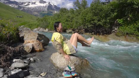 el excursionista relaja las piernas enfriándose en un arroyo de montaña en el tour du mont blanc, rodeado de vegetación y paisajes alpinos
