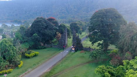 Ancient-stone-gateway-hiding-in-jungle-of-Bali-with-road-in-middle,-aerial-view