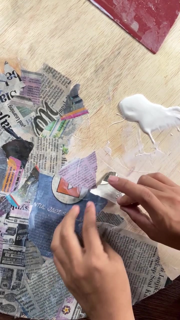 POV verticale 4K a mano libera di mani che incollano ritagli di giornale riciclati su compensato usando colla PVAC. Progetto creativo di riciclo fai-da-te e processo artistico a tecnica mista