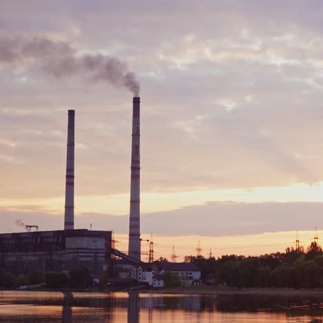 factory in the countryside. industrial zone near the river in the morning. harmful smoke going in the air from manufacturing among evening nature.