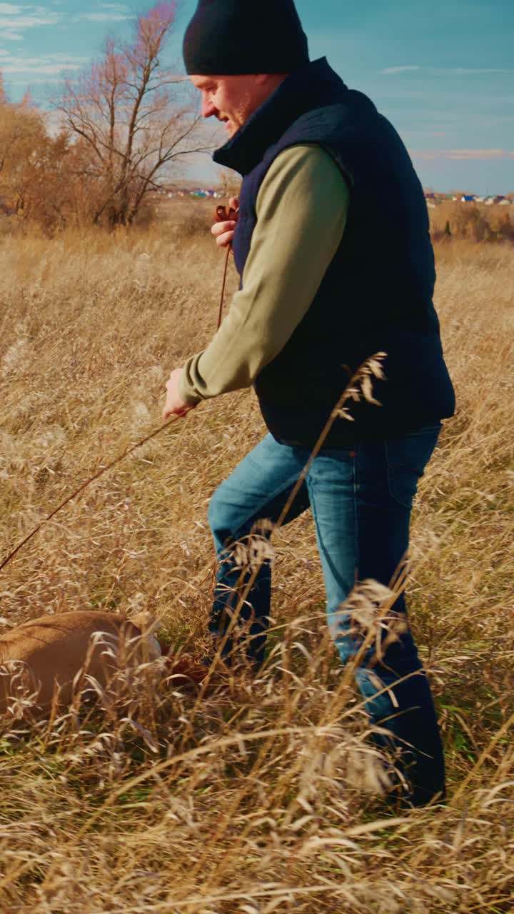 Uma pessoa aproveitando um belo dia ao ar livre enquanto passeia com um cachorro pela grama alta em um cenário natural pitoresco, destacando a alegria da companhia de animais de estimação e aventuras ao ar livre no outono ou inverno