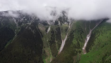 misty mountain peaks with snow, lush green valleys below, aerial view