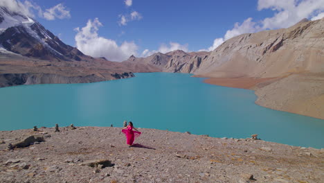 Filmy drone shot reveals Nepal landscape of Tilicho World&#039;s highest Lake, woman in pink dress walks with Heroine feels, cinematic blue sky with clouds 4K
