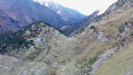 Refuge-Espingo-hiker-shelter-and-Lac-d'Espingo-lake-in-Haute-Garonne,-Pyrénées,-France,-Aerial-dolly-out-reveal-shot