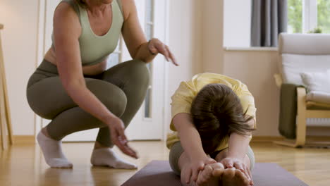 young girl stretching on yoga mat with the help of her trainer