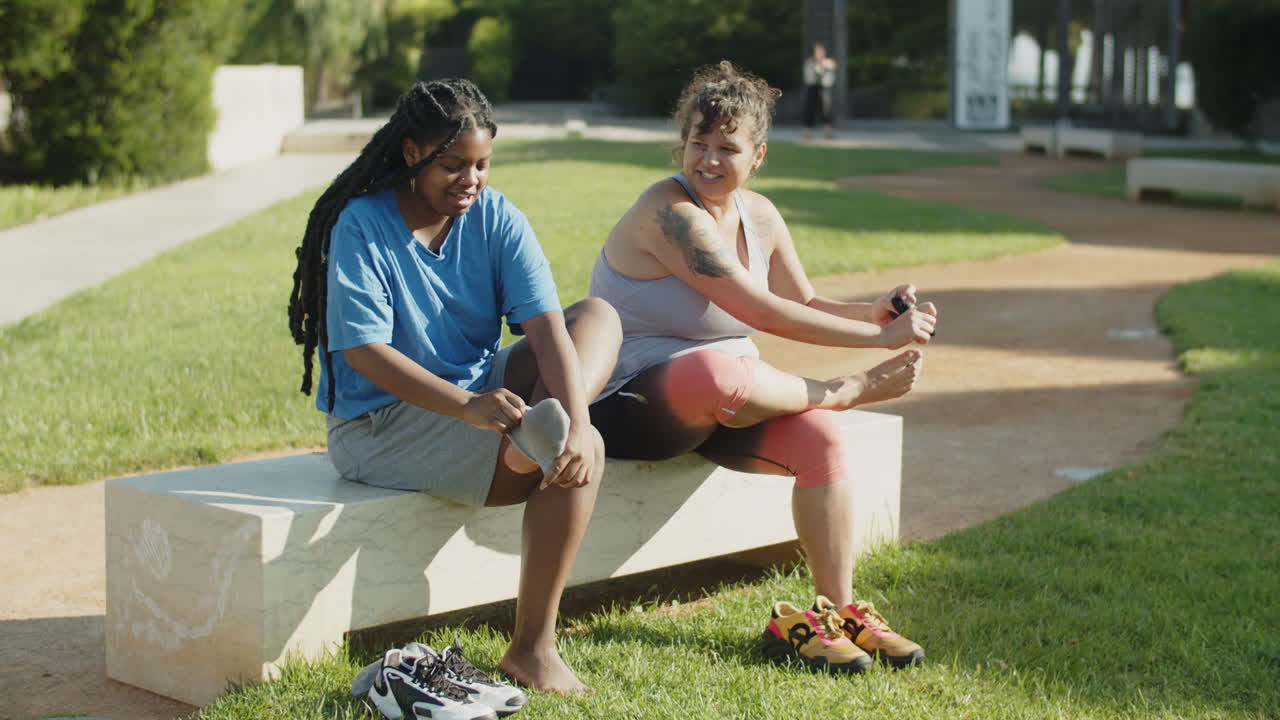 Friends sitting on bench and putting on socks after workout