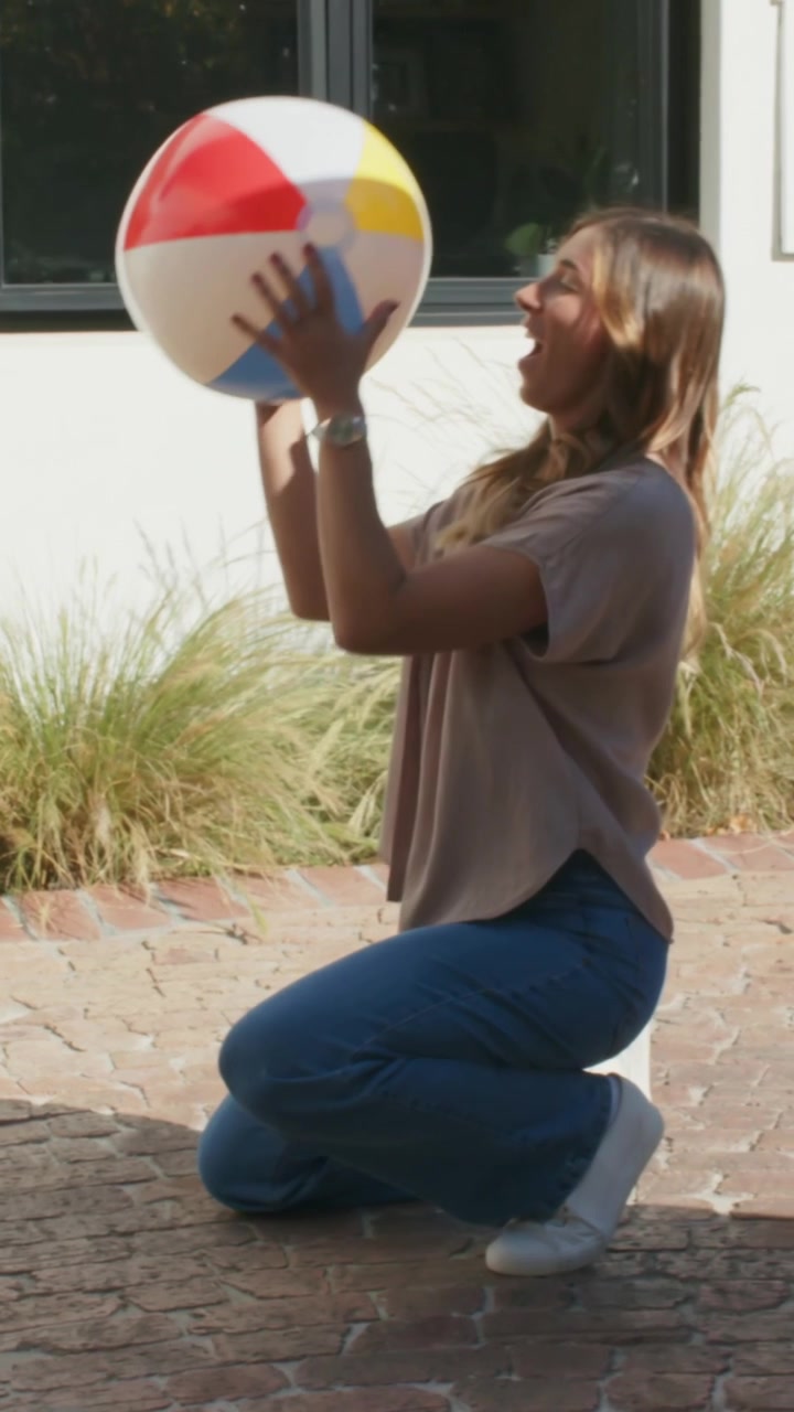 Vertical video: Walking lady pulling case at house, arm taking handle kneeling catching beach ball