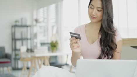 young asian woman entering banking credit card information, purchasing goods or services online or making payments in internet store in application on laptop, concept of ecommerce, comfortable life.