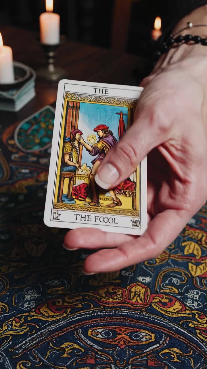 Woman showing the fool tarot card during a tarot reading session on an ornamented tarot cloth, with candles in the background illuminating the scene, creating a mysterious and spiritual atmosphere