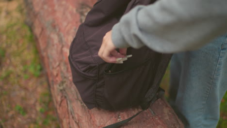숲에서 쓰러진 나무 줄기에 혀있는 검은 배의 클로즈업, 가방이 부분적으로 열리고, 내용물이 드러나고, 평화로운 자연 산책 중에 야외 모험 필수품을 포착합니다.