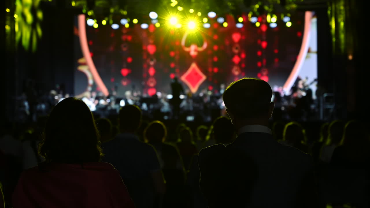 Audience members enjoy an exciting concert as bright lights and colorful visuals fill the stage. The atmosphere is electric with music and energy in the evening setting