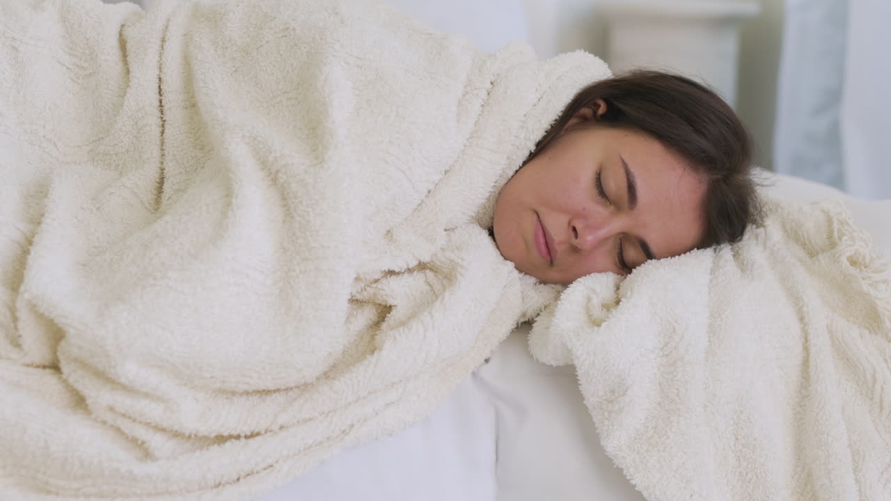 하얀 담요에 싸인 침대에 누워 기침하는 아픈 여자