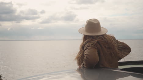 red haired beautiful woman stands up in her car to look out over the beautiful landscape of a lake