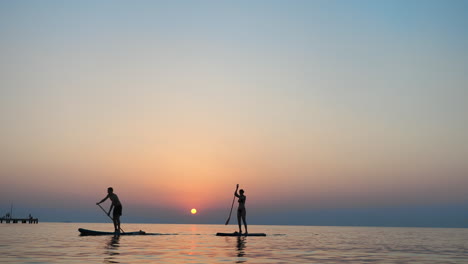 siluetas haciendo paddleboard al atardecer en el mar