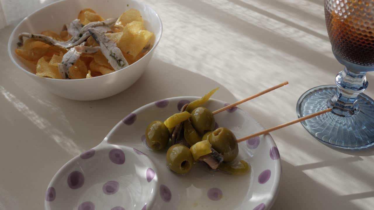 Tapas and vermouth scene with olives, anchovies, chips, and refreshing drink