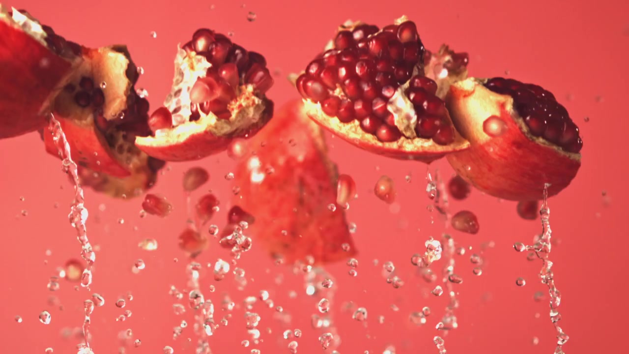 Slowmotion granatæblestykker sprøjter med vand på rød baggrund