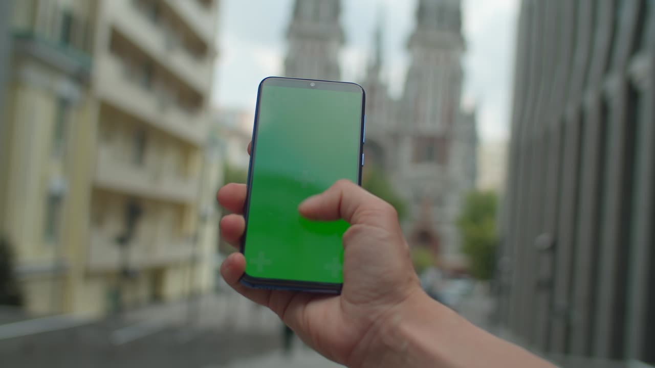 Female hand scrolling mobile phone screen with chromakey on the city street. Woman touching green cellphone screen outdoors.
