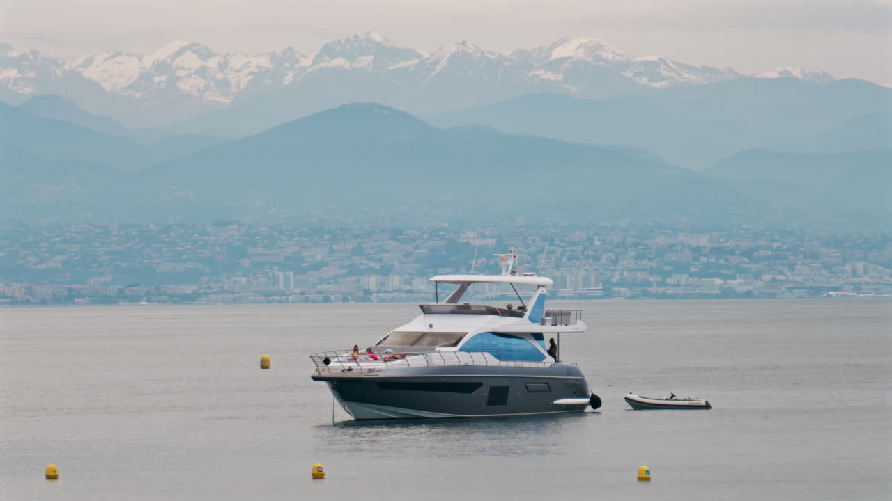 Antibes, France - May 6, 2025: People on a boat docked on the sea with the city and mountains on the background in daylight