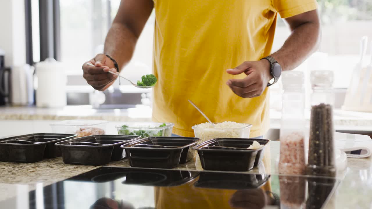 Afrikanischer Mann greift nach Löffel, schöpft Reis, portioniert Gemüse in Behälter für die Essenszubereitung