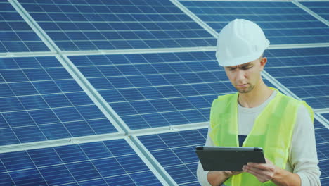 a good-looking worker uses a tablet near ground-based solar panels